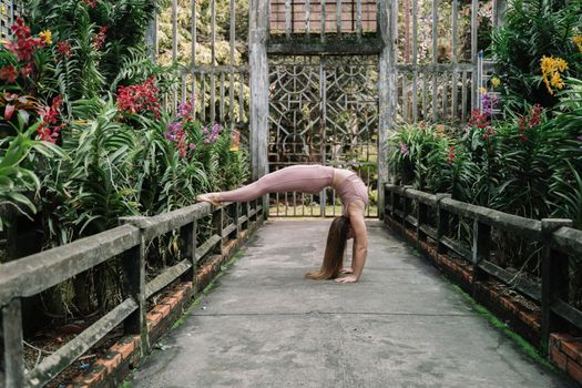 一名女子在宁静的室外花园中，摆出后屈瑜伽姿势，周围环绕着鲜艳的花朵