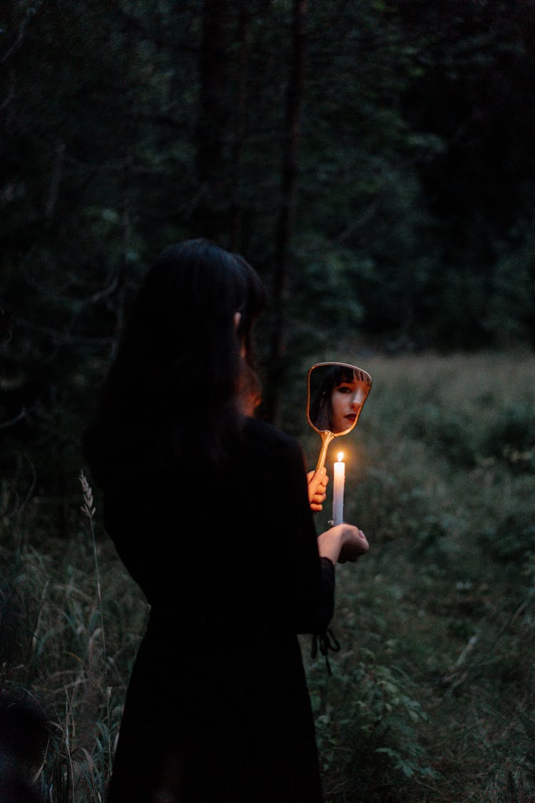 Woman In Black Long Sleeves Dress Holding A Mirror And A Lighted Candle