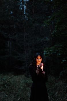 一名年轻女子手持蜡烛，站在黑暗怪异的森林中