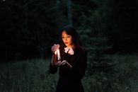 黑暗的森林中，一名年轻女子手持蜡烛，营造出神秘的氛围