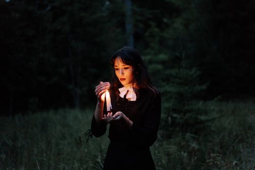 Free A young woman holds a candle in a dark forest, creating a mysterious ambiance. Stock Photo