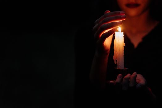 特写中，一个人在黑暗中举着一支点燃的蜡烛，营造出喜怒无常的氛围