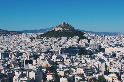Stunning aerial shot of Athens, showcasing Lycabettus Hill amid the city's vast skyline under a clear blue sky.