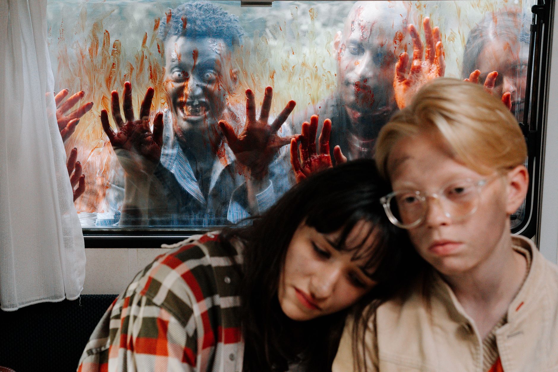 Frightened survivors hide inside while zombies approach the window.