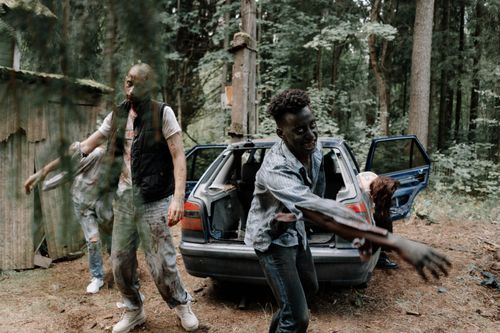 Free A group of zombies walking near an abandoned car in a creepy forest setting. Stock Photo