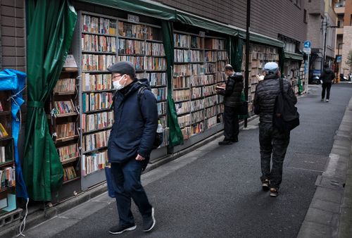 Free People browsing street bookstore in a Tokyo alley, showcasing everyday urban life. Stock Photo