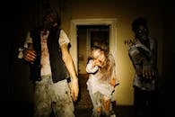 在光线昏暗的废弃房屋中，三个穿着服装的僵尸伸出双手