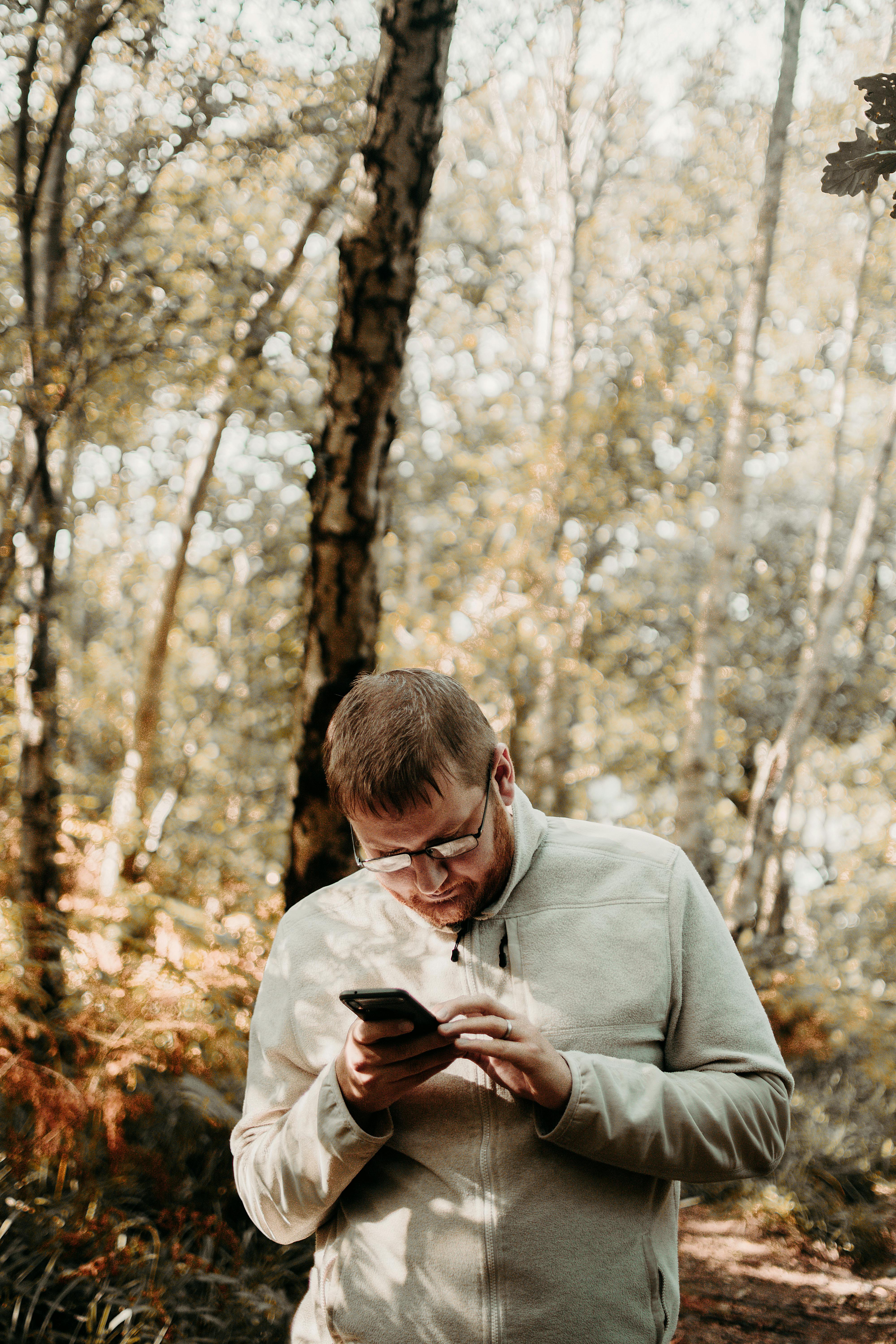 Caucasian man engrossed in smartphone amidst an autumn forest landscape.