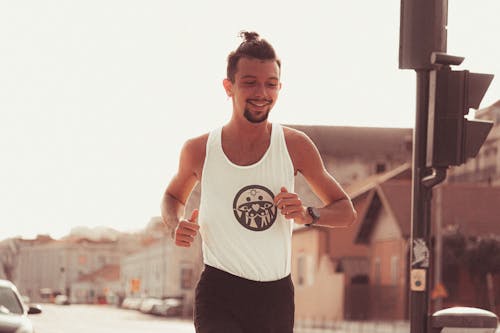 Positive muscular sportsman in activewear jogging along street in sunny day in city