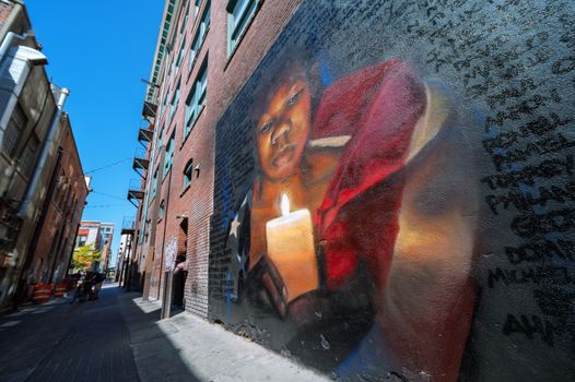 Narrow street with houses with large graffiti depicting black boy with American flag holding burning candle