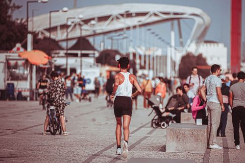 Free Full body back view of anonymous male athlete in headphones jogging along street in sunny crowded park Stock Photo