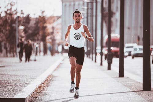 Full body of runner in sportswear jogging along paved pavement in sunny day in city