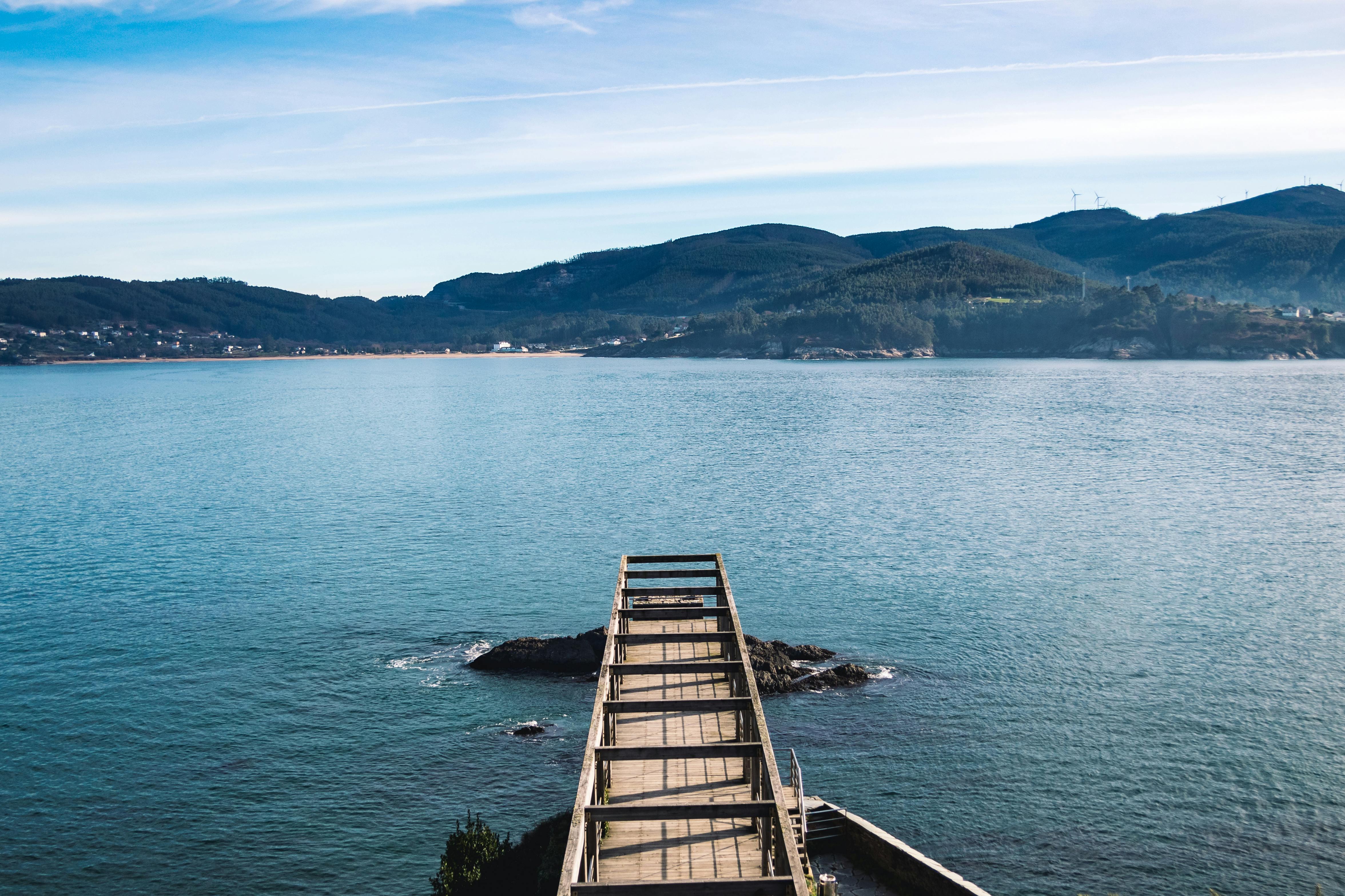 A tranquil pier extends into the waters of Viveiro Bay with lush hills in the background. Perfect for travel and nature imagery.