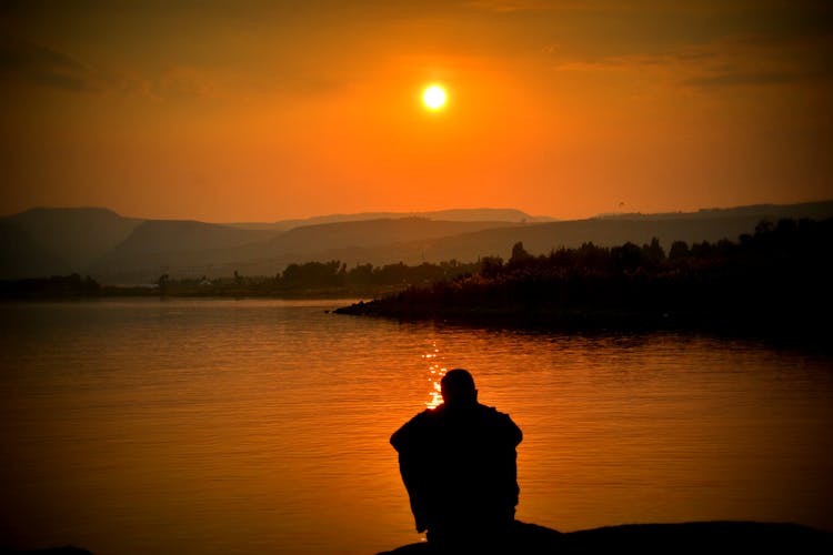 Silhouette Of Person Sitting Beside Body Of Water