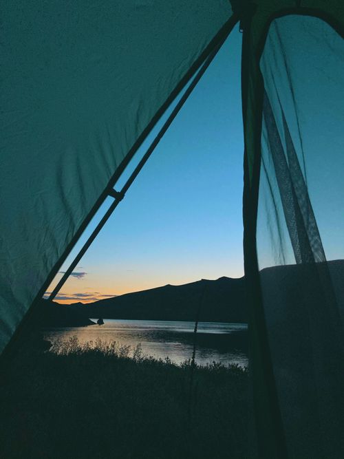 Free Peaceful lake and mountain view at twilight from a tent, ideal for camping and adventure enthusiasts. Stock Photo