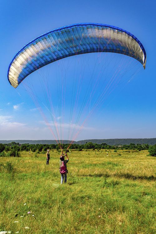 Free Two people preparing to paraglide on a sunny field with clear blue skies. Stock Photo