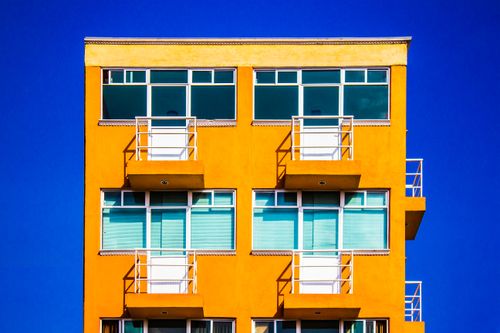 Free Exterior of bright yellow modern building with geometric balconies and windows against cloudless blue sky Stock Photo