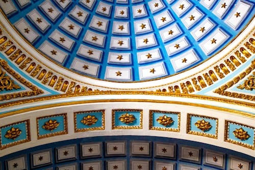 From below of rich decorated ornamental domed ceiling on Catholic basilica with blue and golden elements