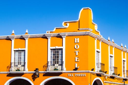 Exterior of aged historical building with bright yellow walls and symmetric balconies against blue sky