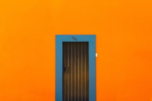 Free Exterior of bright orange wall of building with door with metal casing and drawing in daylight in city street outside Stock Photo