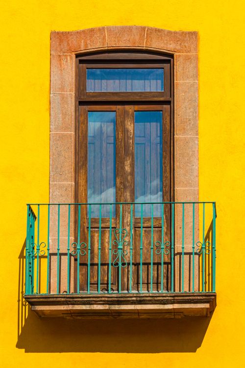 Free Balcony with wooden shuttered door and metal green fence placed on yellow wall of aged building in daylight in street Stock Photo