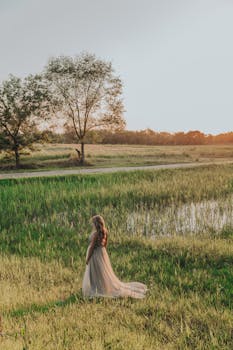 从上面看，一位面目全非的女性穿着带褶边的长裙，在绿树成荫的草地上漫步，阳光洒落其间
