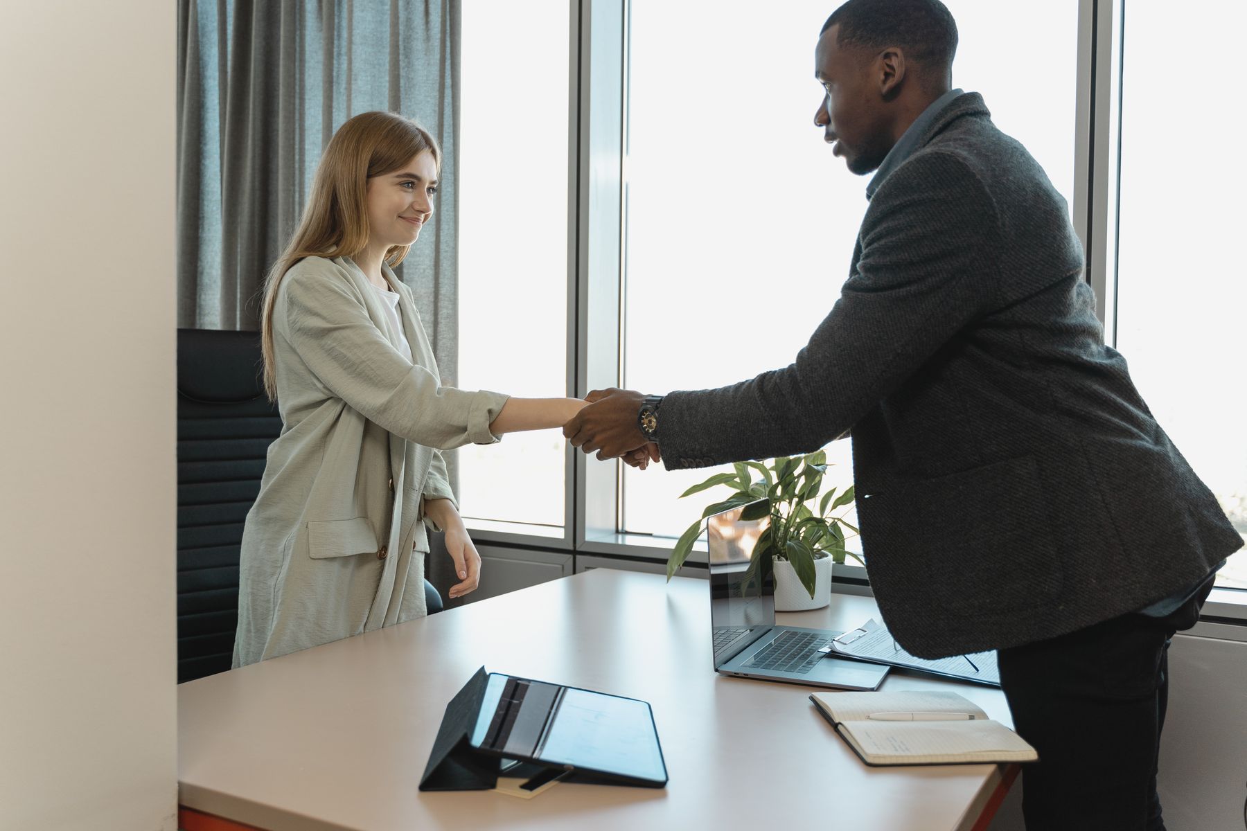 Two business professionals shaking hands across a desk in a bright office