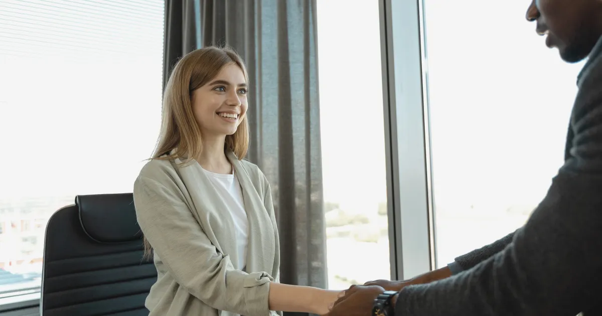 A woman smiling as she shakes hands with a man across a desk, representing Texas TRAIGA biometric AI hiring