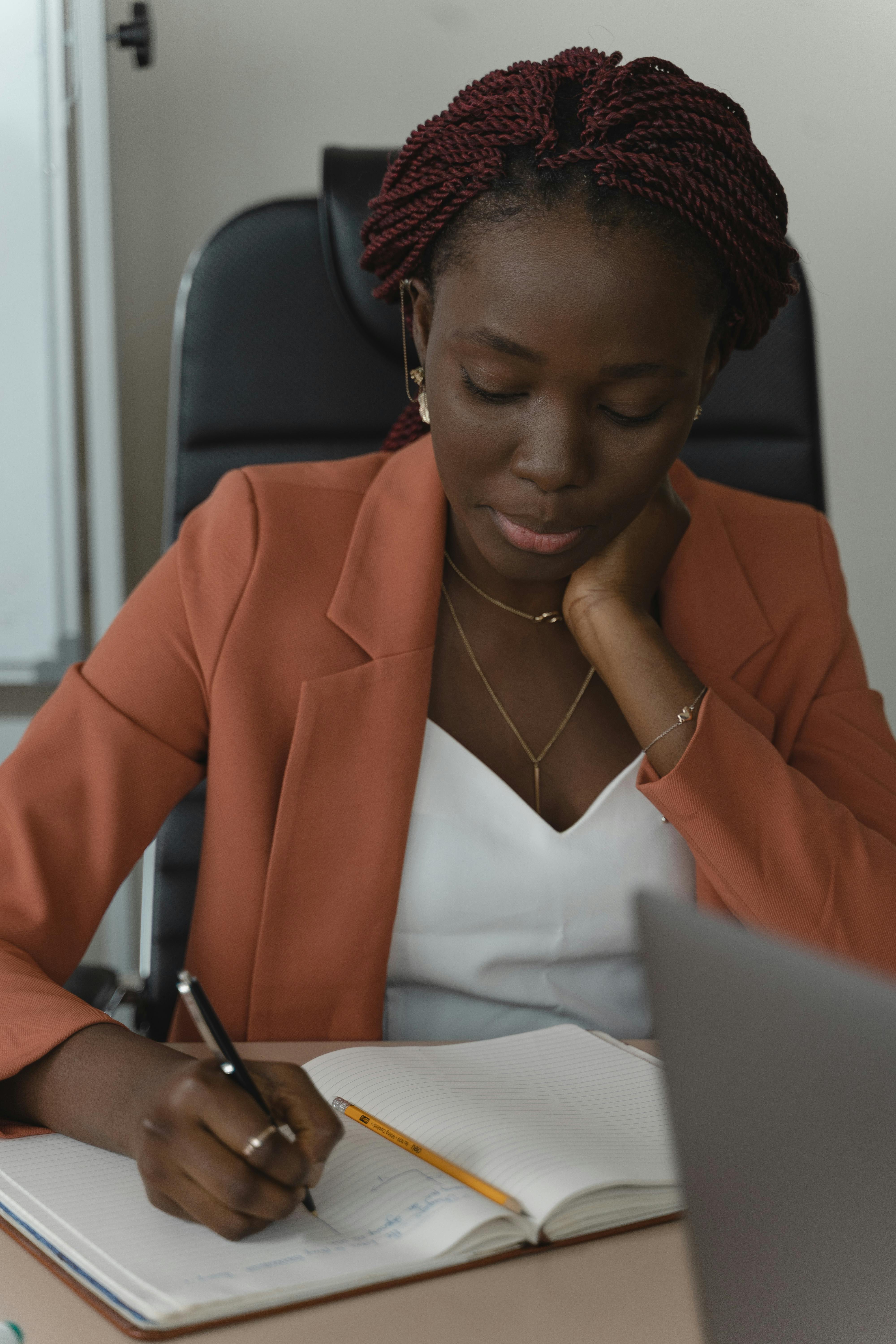 一位穿着西装外套的非裔美国妇女正在工作场所的笔记本上写字