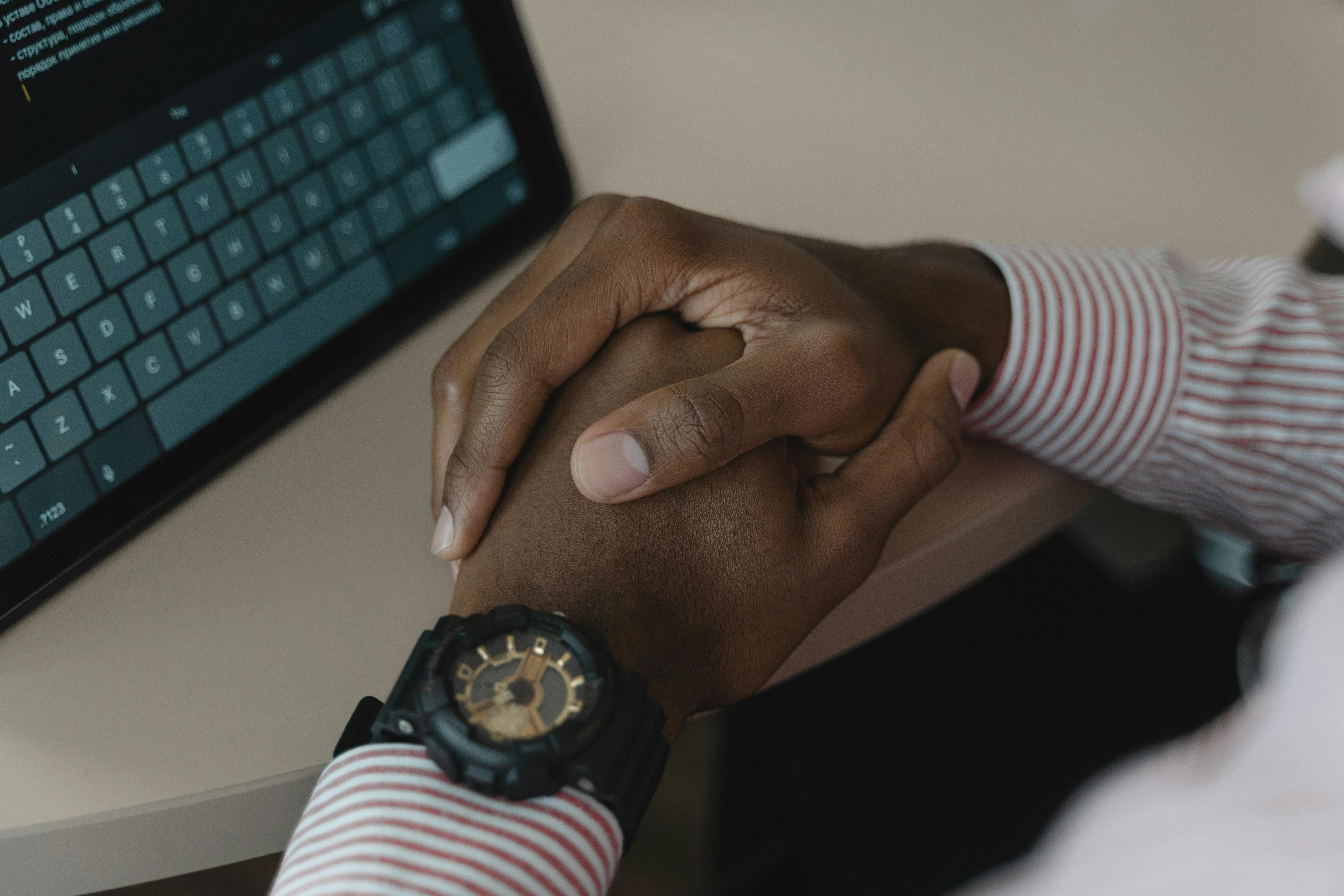 Close-up image of crossed hands wearing a watch near a tablet keyboard.