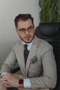 一位专业人士穿着西装、戴着眼镜，自信地坐在现代办公室的办公桌前