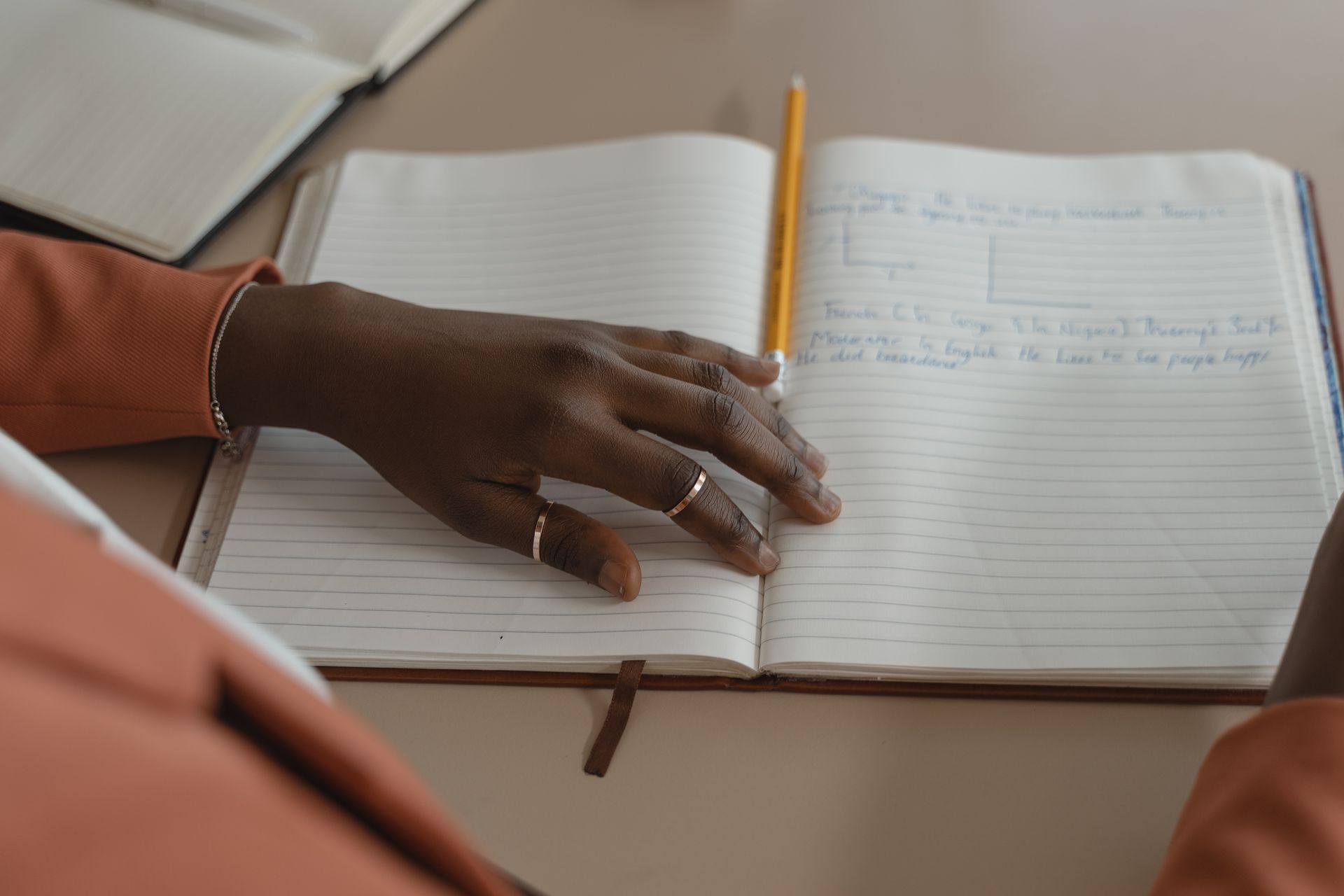 Close-up of a hand writing in a planner with stylish jewelry, creating an ambiance of elegance and preparation.