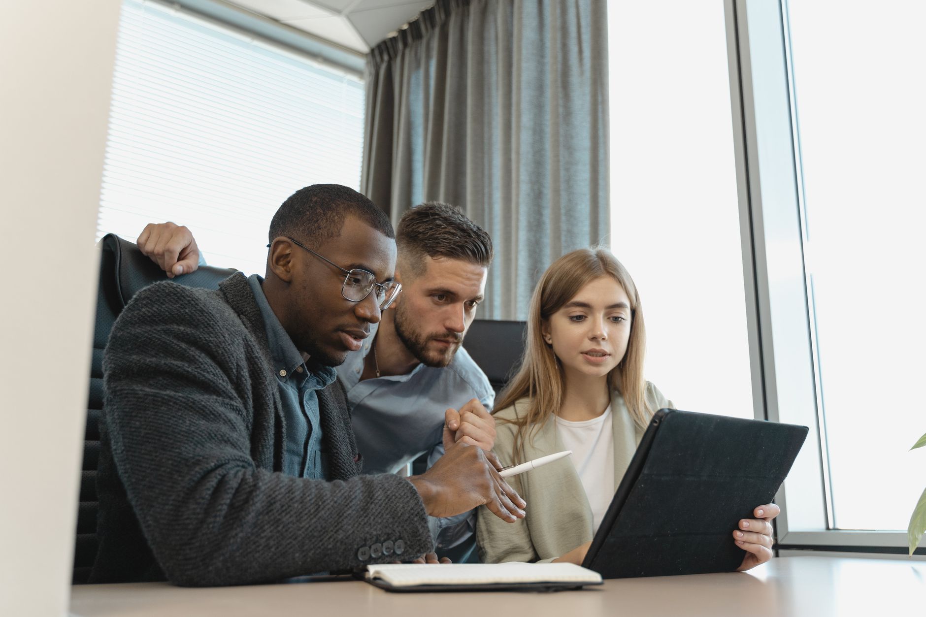 Team of three diverse professionals working on a project with a tablet in a modern office setting.
