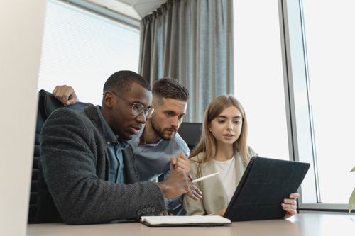 Free Team of three diverse professionals working on a project with a tablet in a modern office setting. Stock Photo