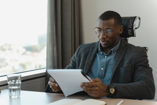 A focused businessman in eyeglasses reviewing documents at his office desk, providing a professional workspace vibe.