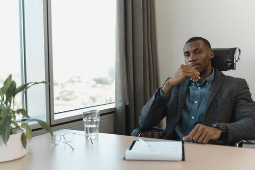 Free Professional man in a thoughtful pose at an office desk with city view. Stock Photo