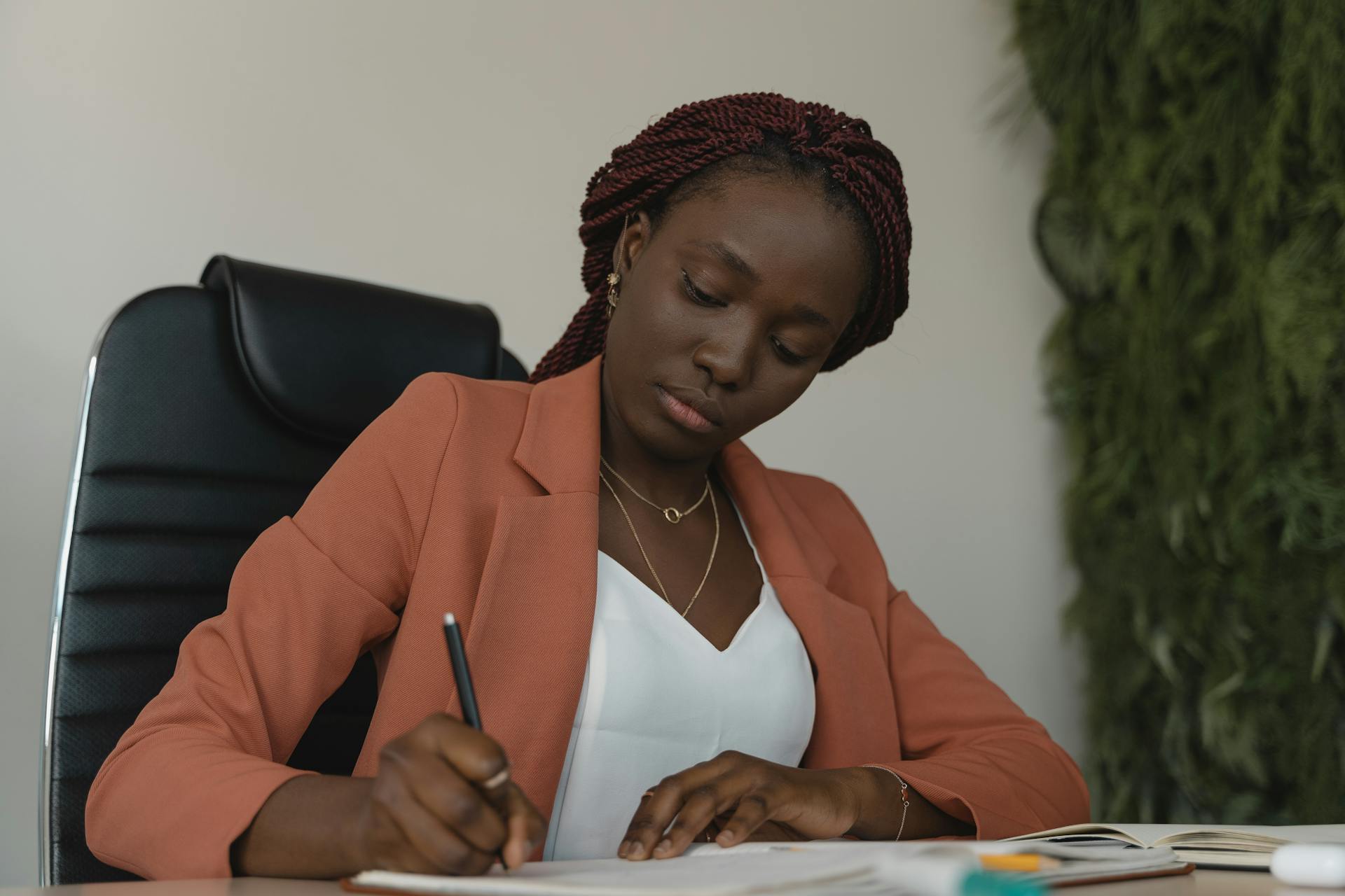 Focused businesswoman writing notes at a desk in a modern office setting.