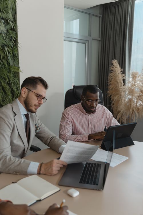 Free Two businessmen working collaboratively in a modern office with laptops and paperwork. Stock Photo