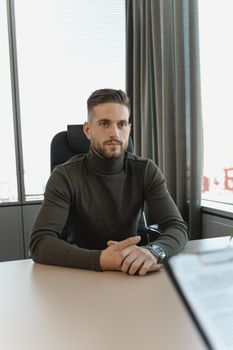 一位表情若有所思的商人，坐在现代办公室的办公桌前