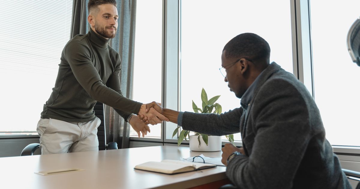 A candidate shaking hands with an employer after a successful interview at an auto repair shop.