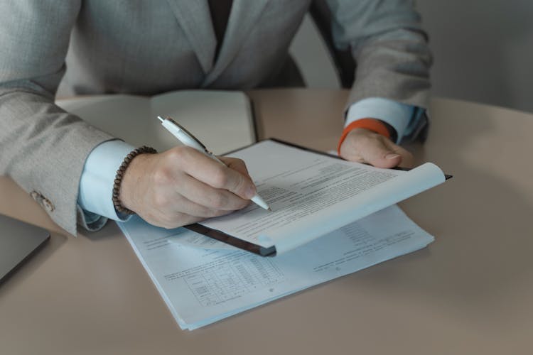 Person In Gray Suit Holding White Pen And Document On A Clipboard