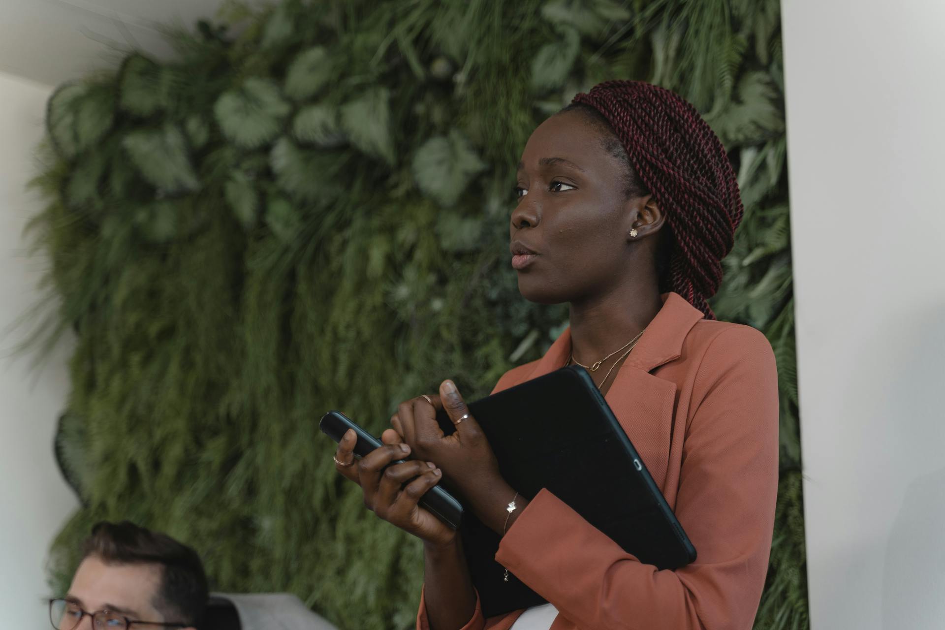 Confident businesswoman holds a tablet while speaking in a modern office setting.