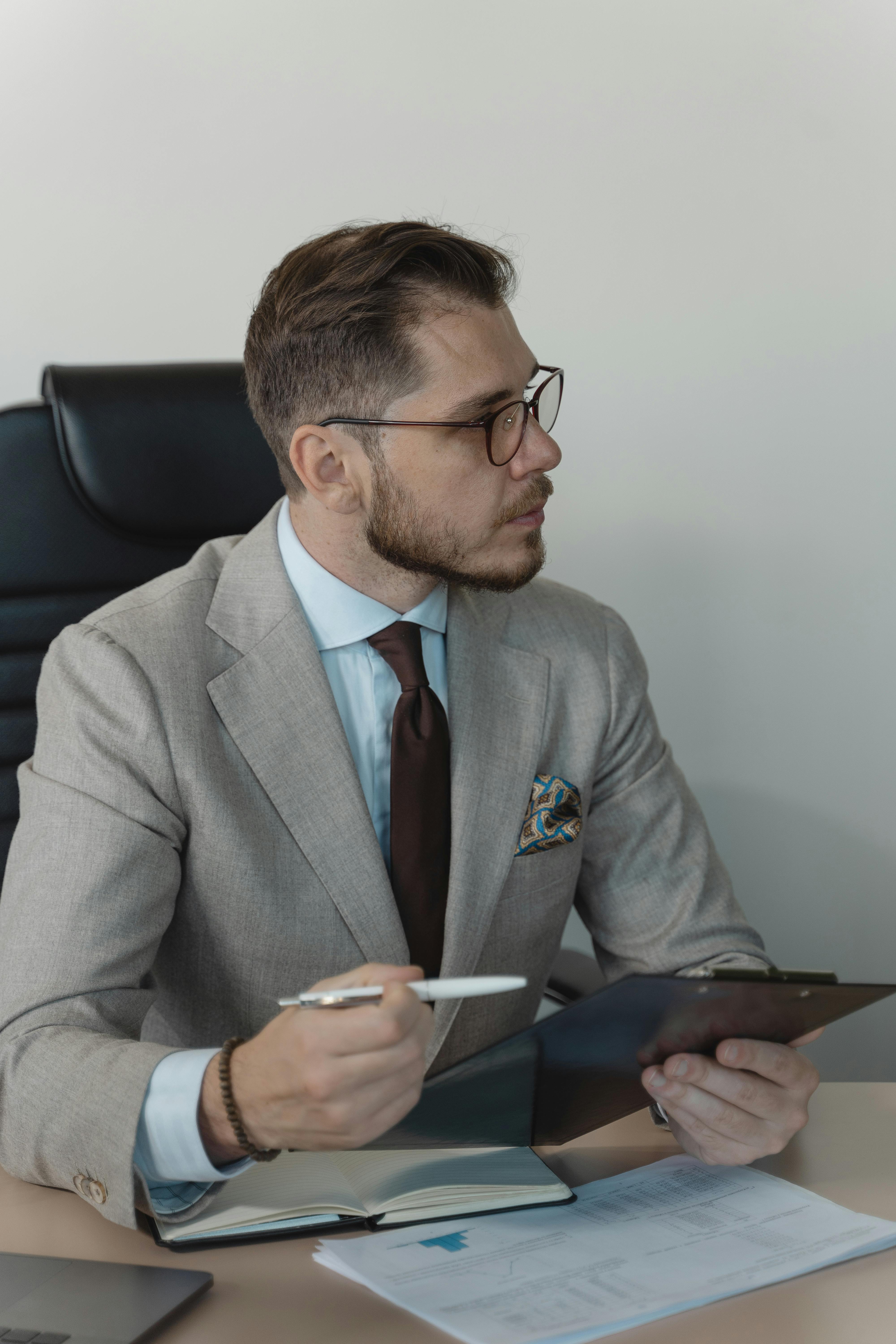 man in gray suit jacket holding clipboard and a pen