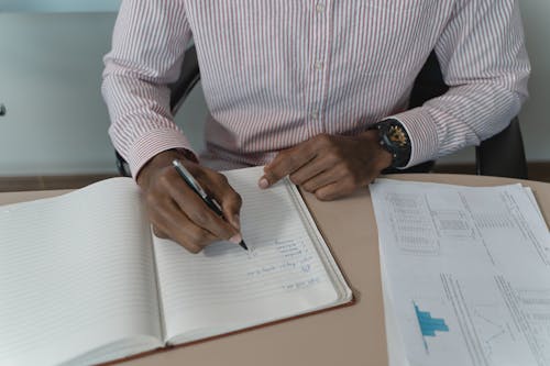 Free A Person in Long Sleeves Writing on a Notebook Stock Photo