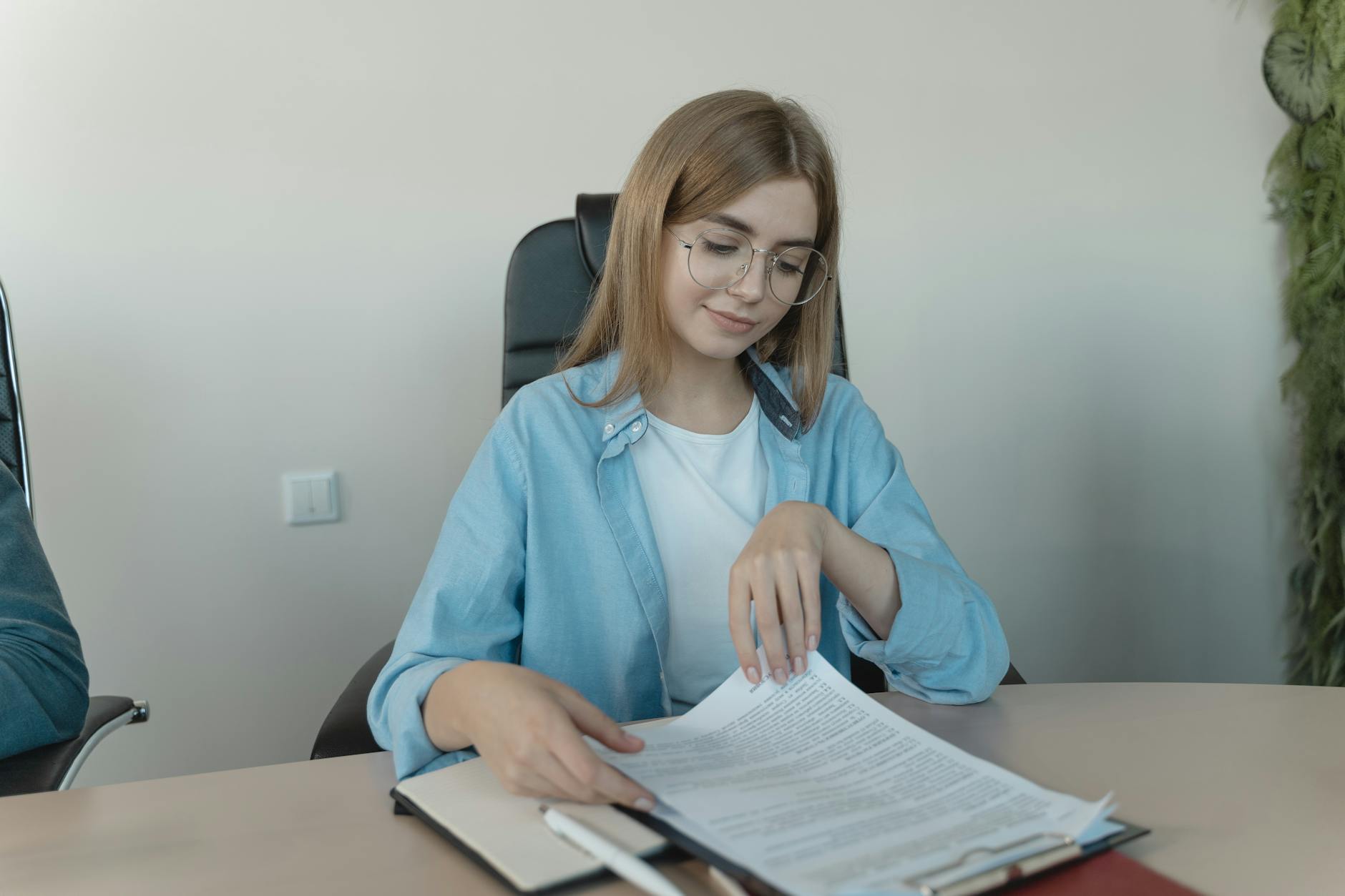 Woman Sitting on an Office Chair while Reading the Document on a Clipboard