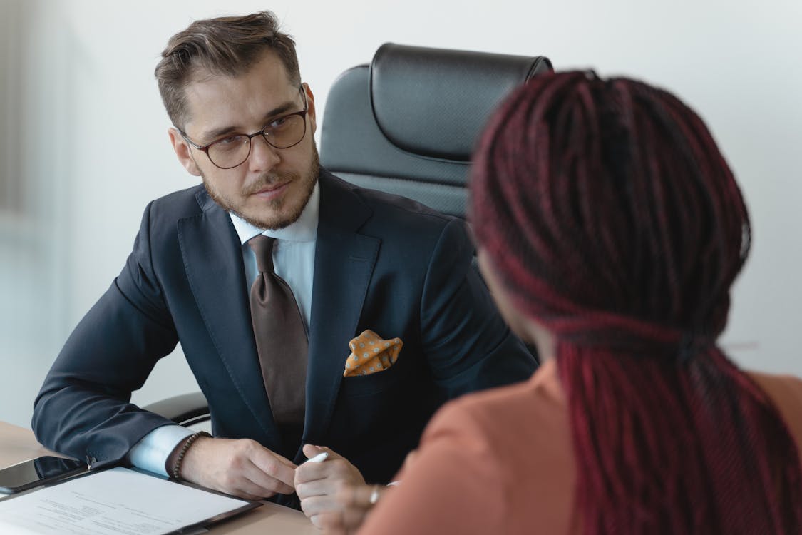 Free Man in Corporate Attire Sitting In front of a Person with Afro Braids Stock Photo