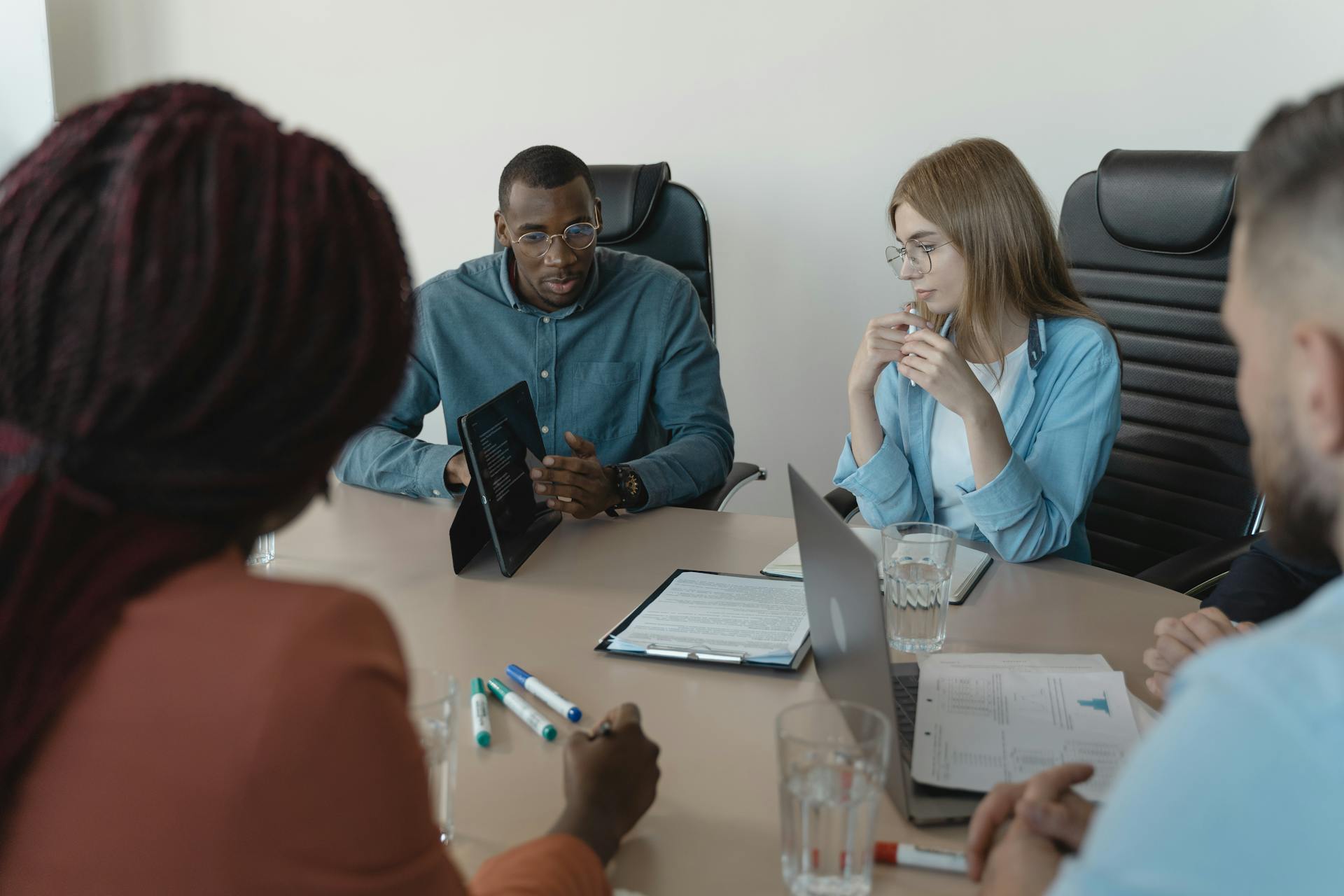 A diverse group of professionals collaborating in an office meeting using digital devices.