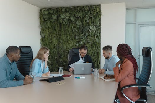 A diverse team brainstorms in a modern office with green wall decor.