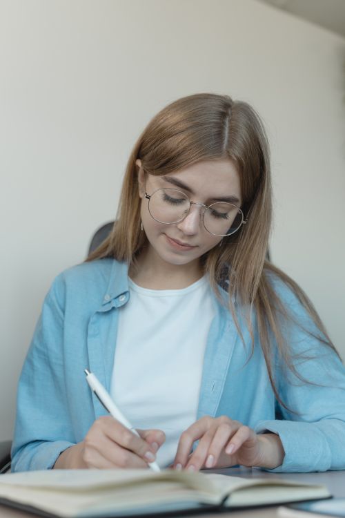 Free Young woman concentrating while writing in a notebook at a desk indoors. Stock Photo
