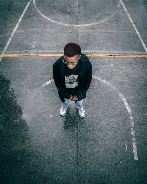 Contemplative black man standing on wet asphalt sports ground